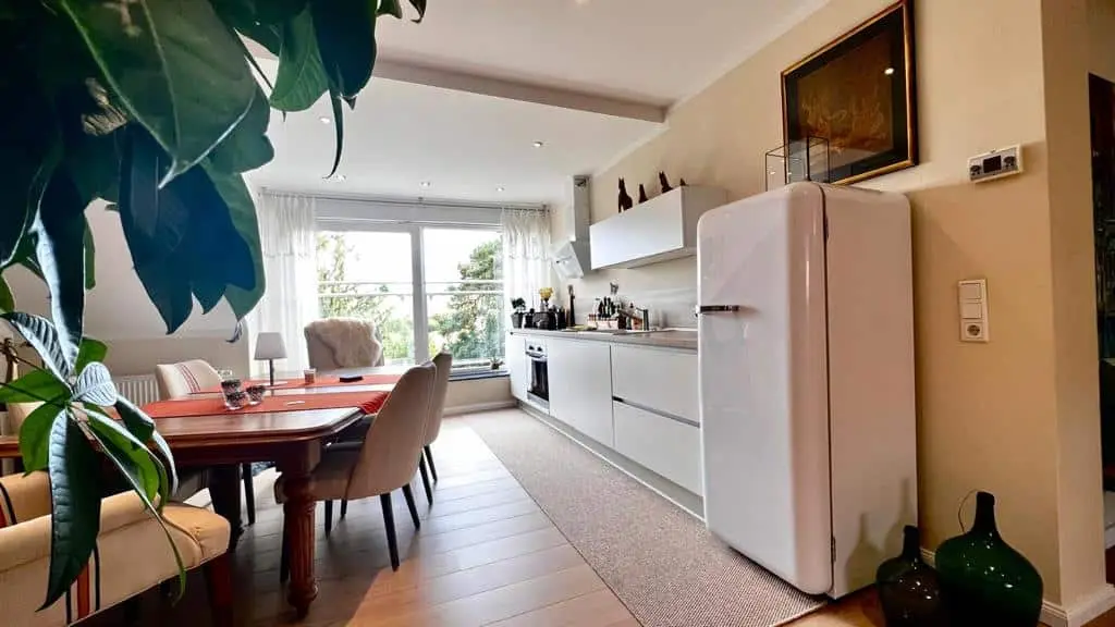 Wohnküche mit weißem Retro-Kühlschrank, Esstisch und Blick ins Grüne