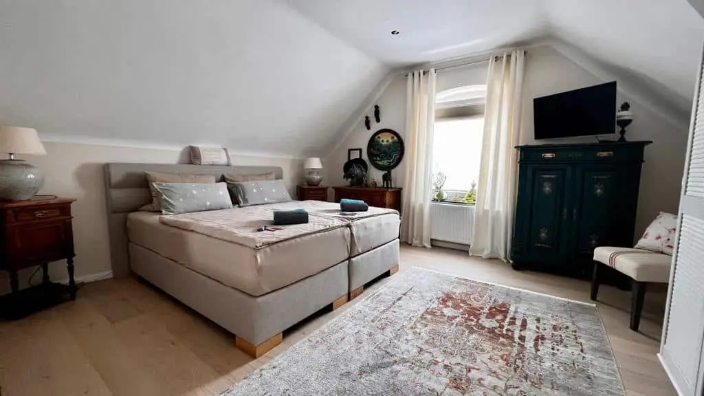 Schlafzimmer unter dem Dach mit Boxspringbett, Rundbogenfenster und antikem grünen Schrank