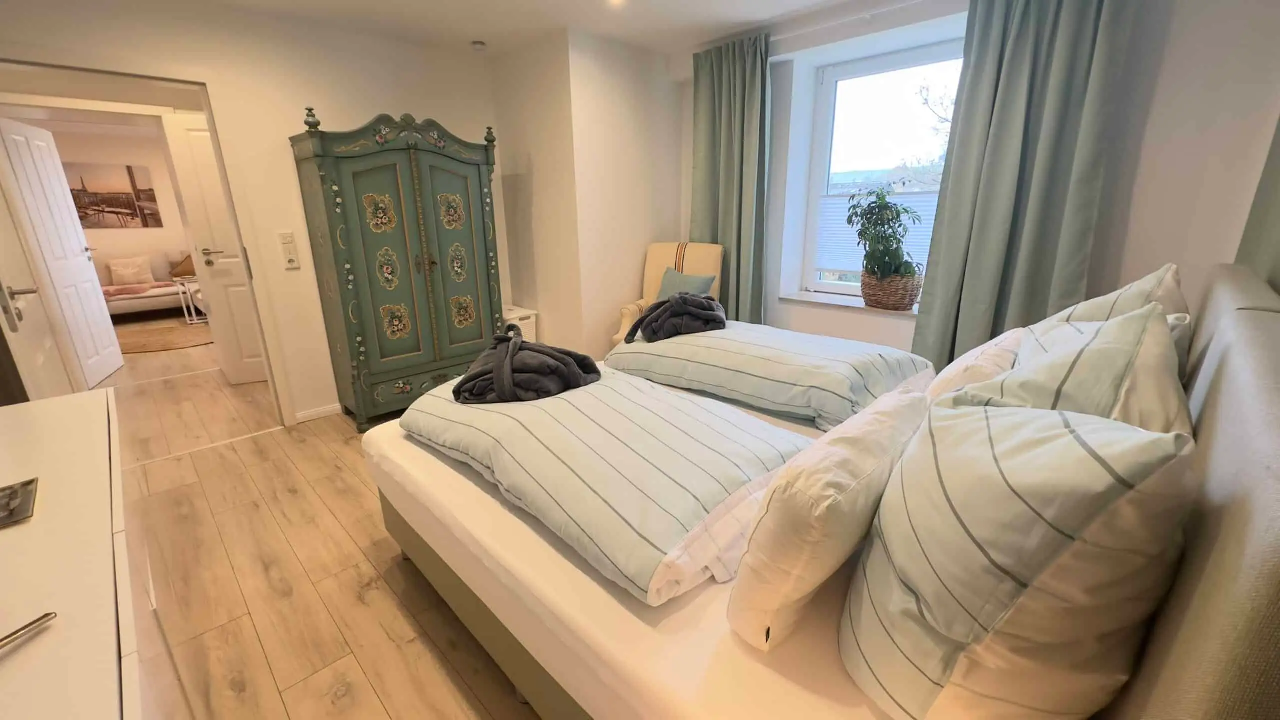 Schlafzimmer mit bemaltem grünen Bauernschrank und zwei Betten am Fenster