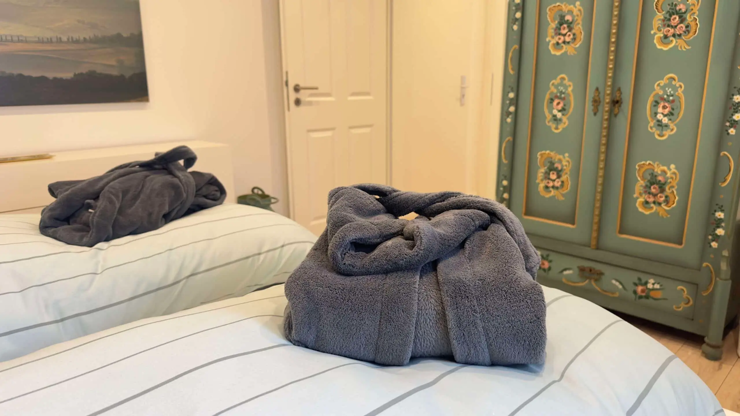 Bademäntel auf den Betten, dahinter der bemalte Bauernschrank